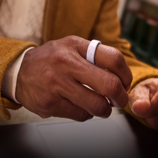 Nahaufnahme der Hand einer Person mit einem Petal Oura Ring 4 Ceramic am Finger