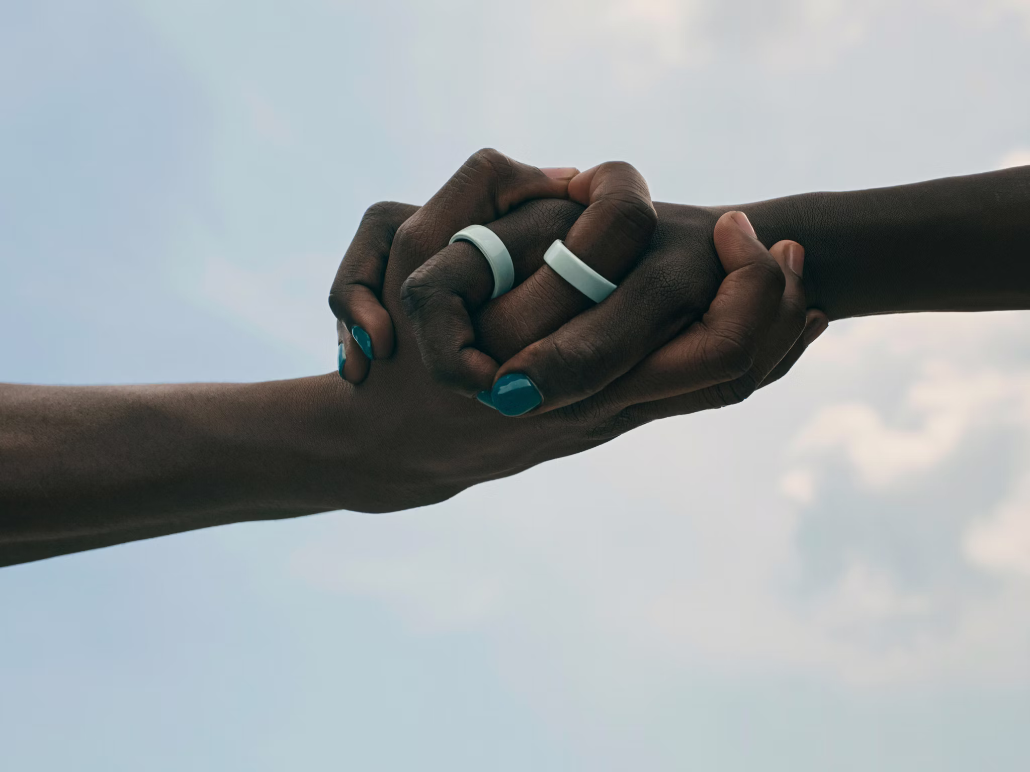 Nahaufnahme von zwei Händen, die sich verschlungen halten und an deren Zeigefingern jeweils ein Oura Ring 4 Ceramic steckt.