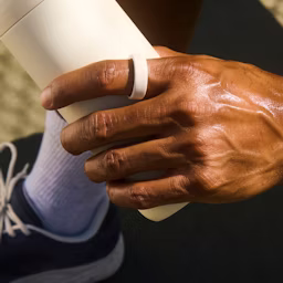 Eine Person, die einen Cloud Oura Ring 4 Ceramic trägt, hält eine Wasserflasche